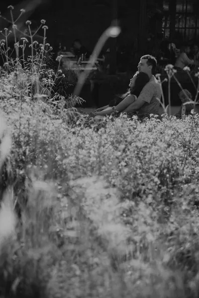 Um casal sentado na relva alta entre flores silvestres, a preto e branco — Olesia Shelkovenko