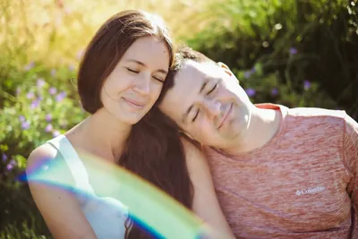 Um casal deitado na relva, cabeças encostadas, com reflexo de sol no enquadramento — Olesia Shelkovenko