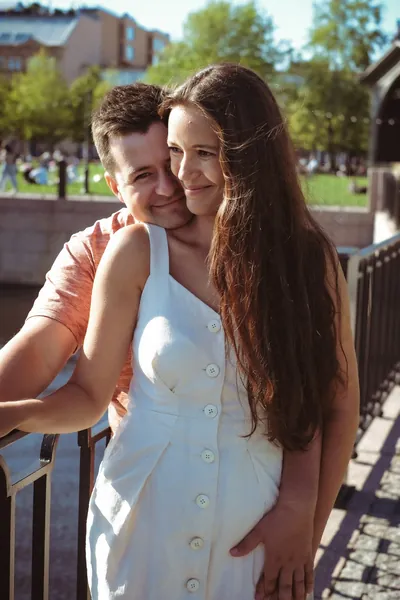 O casal junto a um gradeamento, ela de vestido branco, ele a abraçá-la por trás — Olesia Shelkovenko