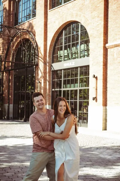 O casal abraçado numa rua da cidade, junto a um edifício de tijolo vermelho — Olesia Shelkovenko