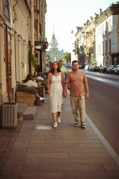 O casal a caminhar pelo passeio, com uma torre da cidade ao longe — Olesia Shelkovenko