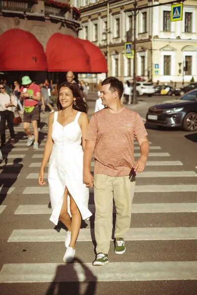 O casal a atravessar a estrada, com toldos vermelhos de café ao fundo — Olesia Shelkovenko